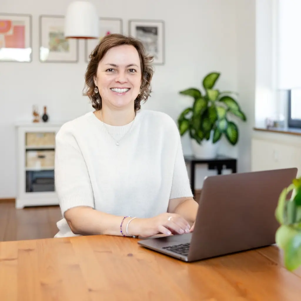 Friederike Ruffmann Oliveira, Online Bussines Assistenz, sitzt lächelnd am Schreitisch vorm Laptop